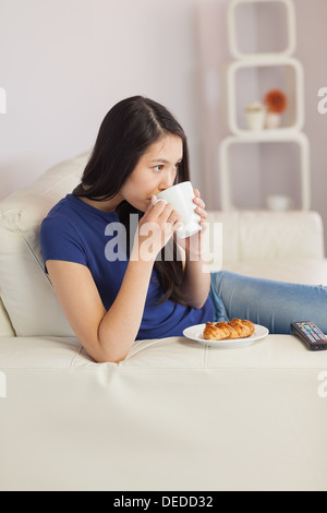 Woman sitting on the sofa drinking coffee with a pastry Stock Photo