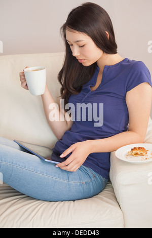 Young woman using her tablet pc and holding mug of coffee Stock Photo
