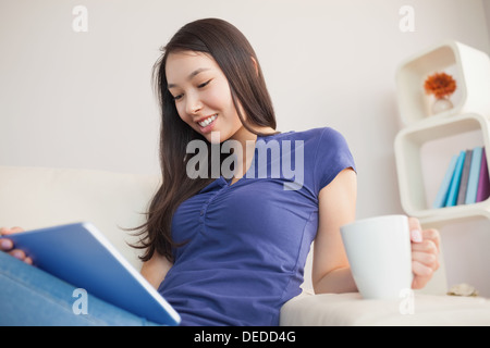 Young attractive asian woman using her tablet pc and holding mug of coffee Stock Photo