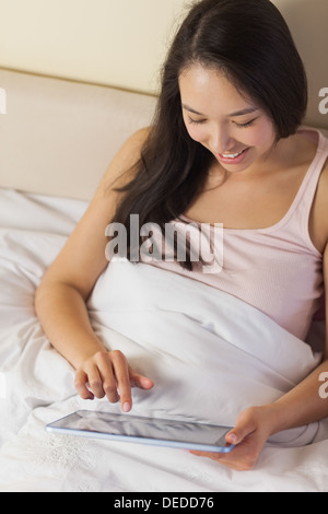 Cheerful young asian woman sitting in bed using her digital tablet Stock Photo