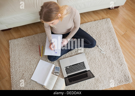 Young woman doing homework and sitting on floor using laptop Stock Photo