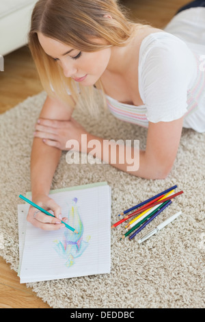 Happy young woman lying on floor sketching on paper Stock Photo