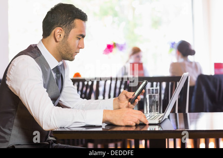 Serious businessman using phone while working on laptop Stock Photo