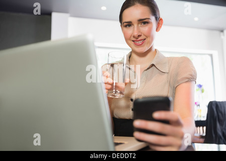 Smiling businesswoman holding glass of water and phone in a cafe Stock Photo