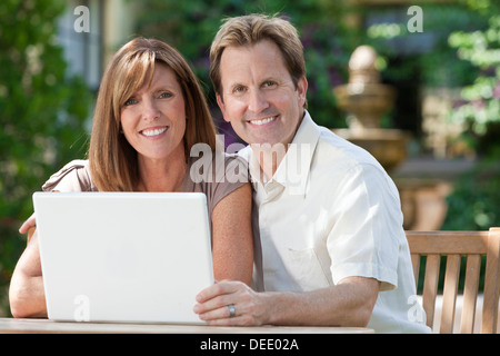 Happy middle aged man & woman couple in their thirties, sitting togEther outside in a garden using a laptop computer Stock Photo