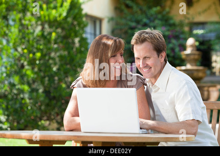 Happy successful middle aged man and woman couple in their thirties sitting together outside in a garden using a laptop computer Stock Photo