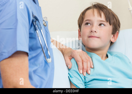 Female doctor or nurse comforting a young boy child in a hospital bed Stock Photo