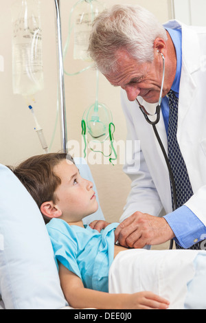 Senior male doctor with stethoscope examining a young boy child in a hospital bed Stock Photo