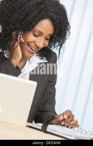 Portrait of beautiful middle aged African American woman or businesswoman using her cell phone and laptop computer in an office Stock Photo