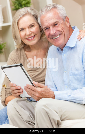 Happy senior man and woman couple sitting together at home smiling and happy using a tablet computer Stock Photo