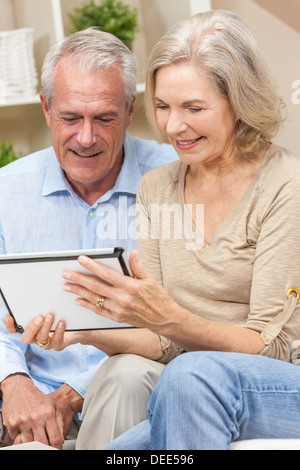 Happy senior man and woman couple sitting together at home smiling and happy using a tablet computer Stock Photo