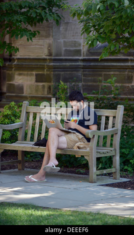 Yale University student listens to music on his smartphone while using his laptop computer. Stock Photo
