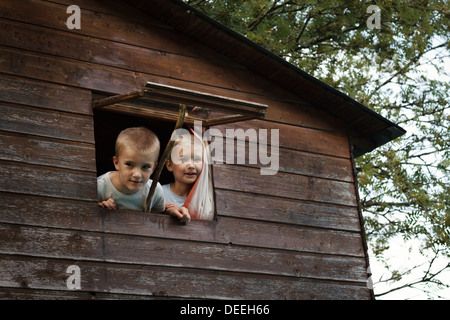 Two boys (4-7) looking out hut window, France. Stock Photo