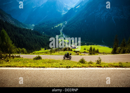 Motorcyclist riding on road pass through mountainous village, beautiful green forest, extreme transport, tour along Europe Stock Photo