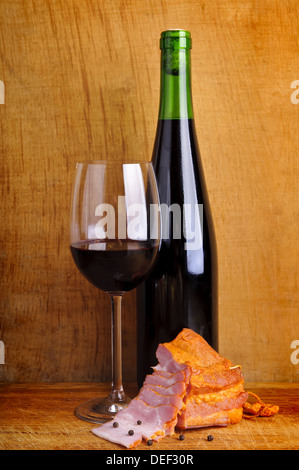 still life composition with glass and bottle of red wine and smoked ham on a vintage wooden backround Stock Photo