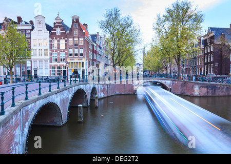 Long exposure of a tourist boat crossing canals Keizersgracht from Leidsegracht at dusk, Amsterdam, Netherlands, Europe Stock Photo