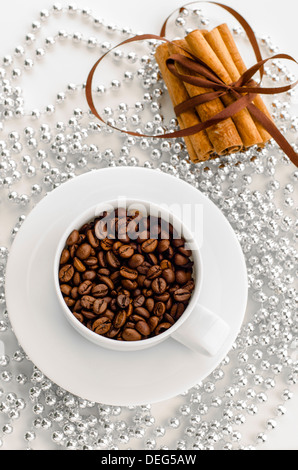 cup with coffee beans and cinnamon sticks tied with brown ribbon on a background of silver beads Stock Photo
