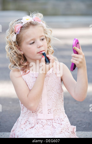 Pretty seven year old girl wearing pink and applying lipstick Stock Photo