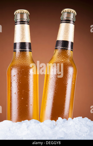 Two beer bottles sitting on ice over a brown background. Stock Photo