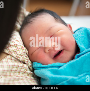 Newborn Asian baby girl smiling and fall asleep in mother's arms, inside hospital room Stock Photo