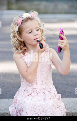 Pretty seven year old girl wearing pink and applying lipstick Stock Photo