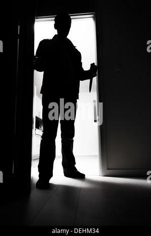 Full-length thief with knife entering into dark room Stock Photo