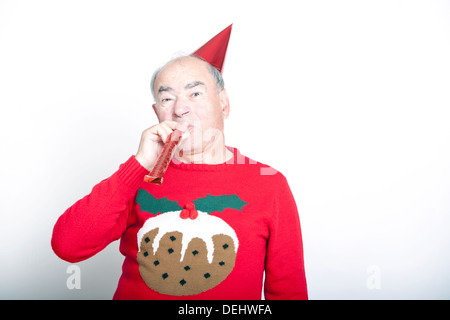 Senior adult man wearing Christmas jumper blowing party blower Stock Photo