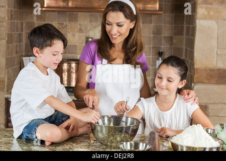 An attractive smiling family of mother and two children, girl boy, son daughter, baking in a kitchen at home Stock Photo