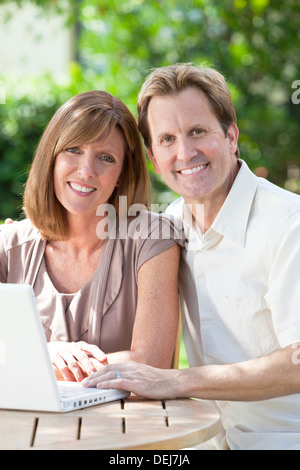 Attractive, successful and happy middle aged man and woman couple in their thirties in a garden using a laptop computer Stock Photo