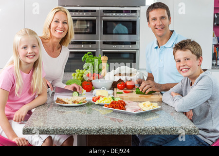 An attractive happy, smiling family of mother, father, son and daughter preparing and eating healthy food in kitchen at home Stock Photo
