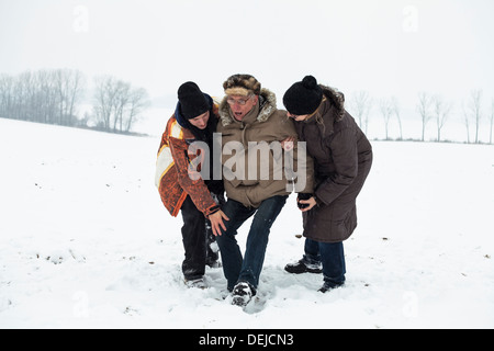 Couple of young people helping to senior man stand up after accident on snow in winter. Stock Photo