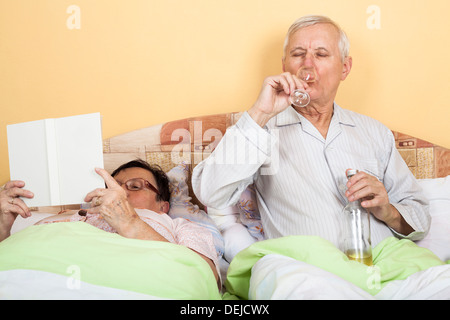 Retired couple relaxing in bed with alcohol and book Stock Photo