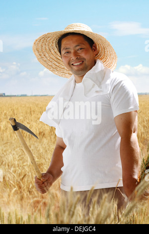 Farmer holding scythe in wheat field Stock Photo