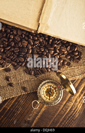 Coffee beans and compass on open book on jute canvas texture. Stock Photo