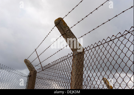 Fence topped with barbed wire on a gloomy and cloudy day Stock Photo