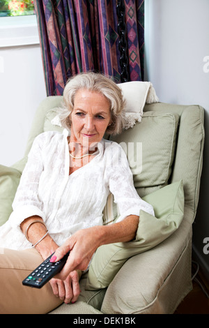 Senior woman changing channels with remote control on armchair home Stock Photo