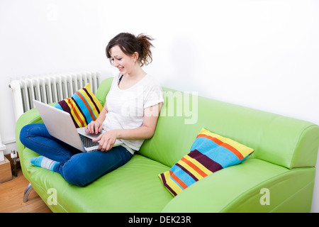 Full length happy young woman using laptop while sitting on green sofa Stock Photo