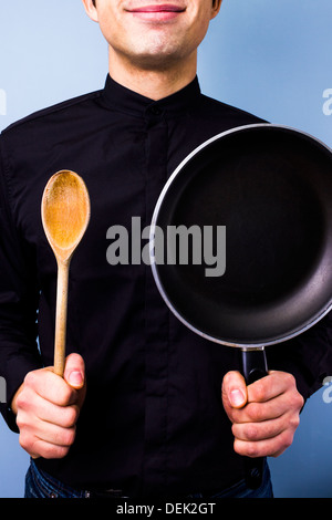 Happy young cook holding a frying pan and a wooden spoon Stock Photo
