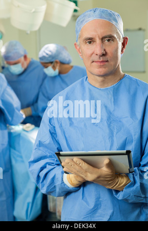 Senior male doctor surgeon using tablet computer with interracial surgical team and patient in hospital operating theater Stock Photo