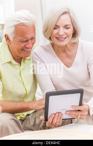 Happy senior man and woman couple sitting together at home on a sofa using a tablet computer Stock Photo
