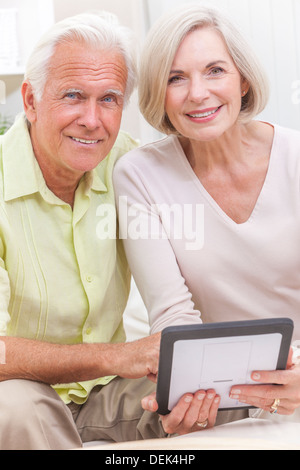 Happy senior man and woman couple sitting together at home on a sofa using a tablet computer Stock Photo