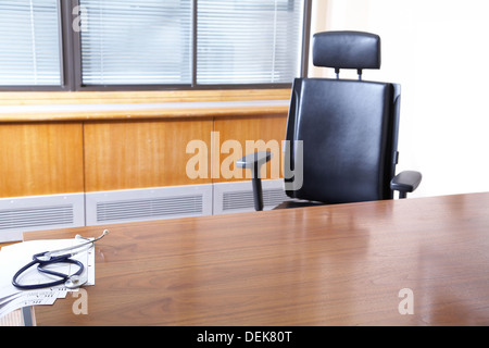 A black leather chair with desk in an empty Doctors office with stethoscope on the table. Stock Photo