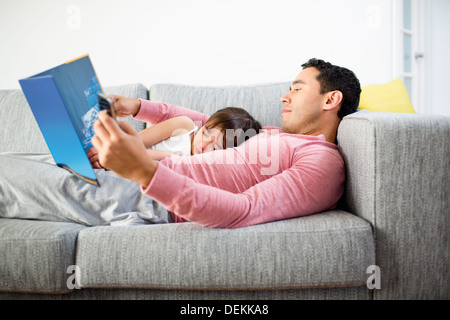 Father and daughter reading together on sofa Stock Photo