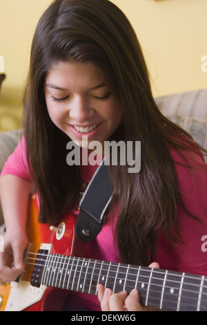 Hispanic girl playing guitar on sofa Stock Photo