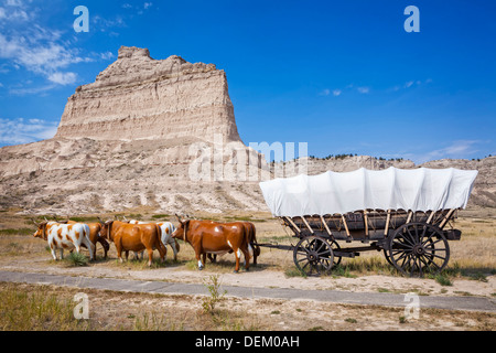 Oxen pulling covered wagon by rock formation, Scott's Bluff National Monument, Nebraska, United States Stock Photo