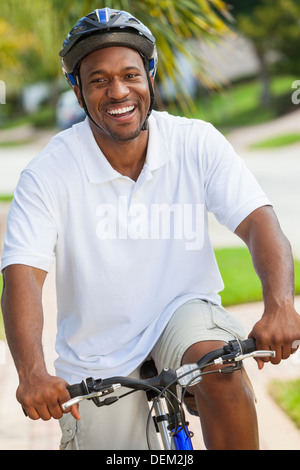 A happy African American man riding his bicycle outside wearing shorts, helmet and polo t-shirt Stock Photo