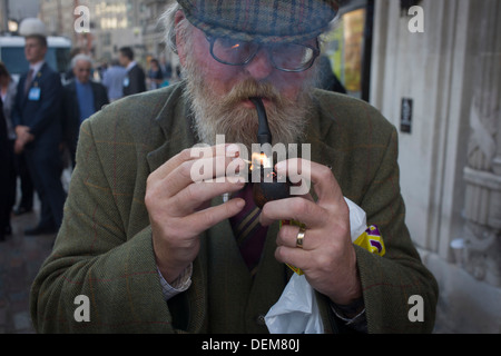 A man in his seventies lights his pipe in a central London street. Stock Photo