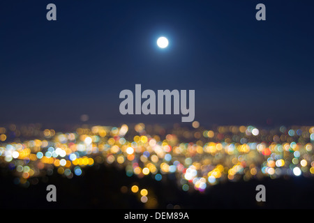 Harvest Full Moon Rise Over Blurred Defocused City Building Lights Landscape at Evening Blue Hour Stock Photo