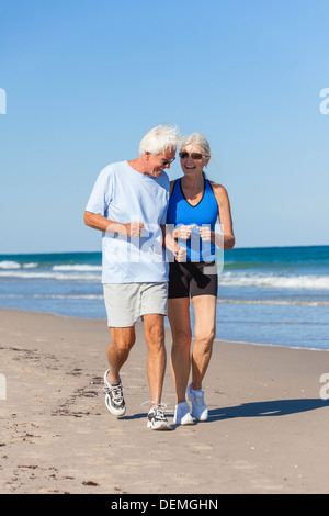 Happy senior man and woman couple together running or jogging by sea on a deserted tropical beach with bright clear blue sky Stock Photo