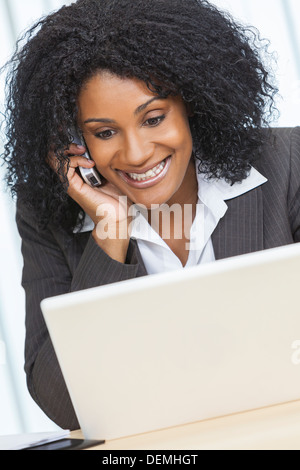 Happy beautiful middle aged African American woman or businesswoman smiling using a cell phone and laptop computer Stock Photo